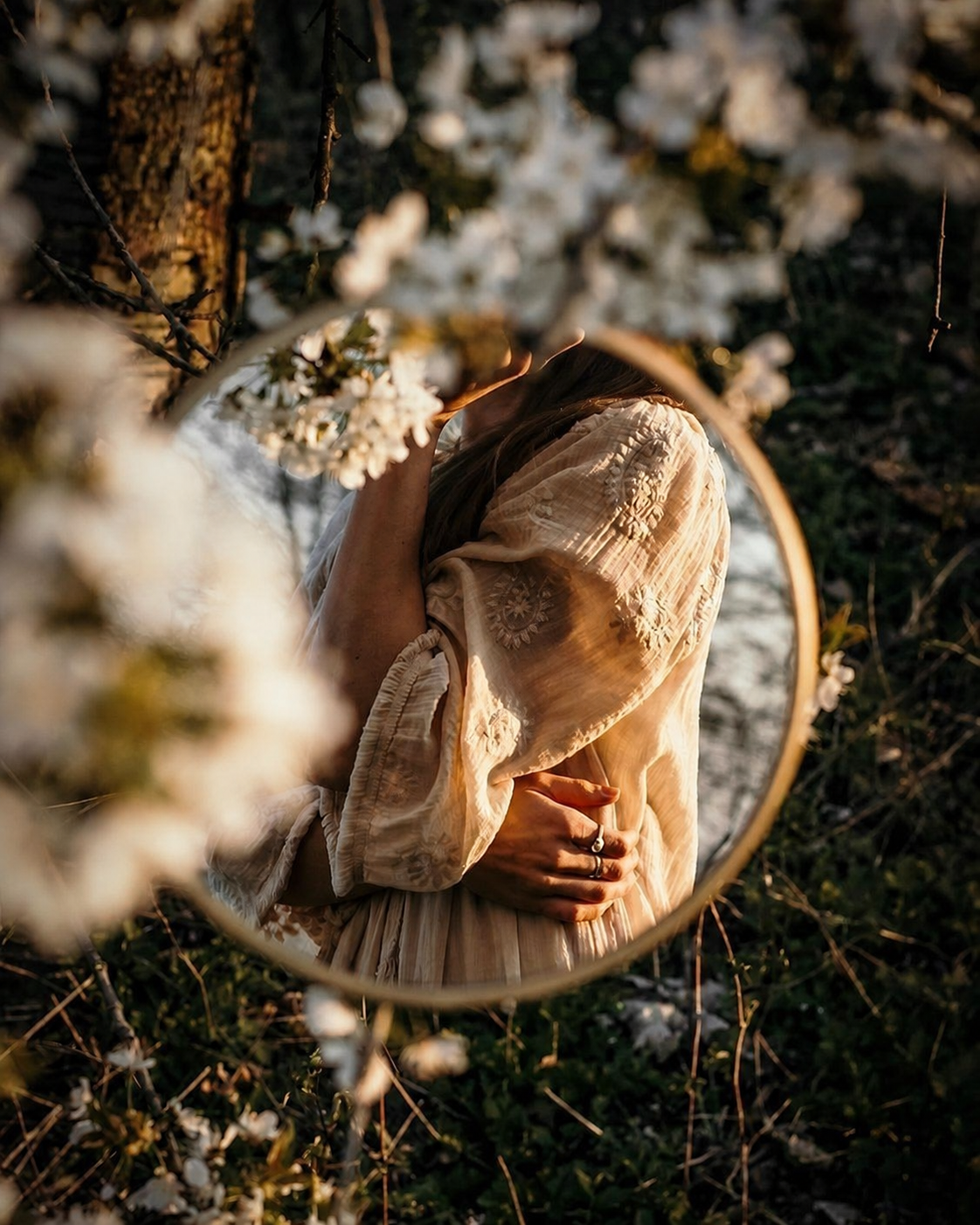 A dark-haired woman reflected in a mirror among flowers.